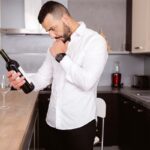 handsome young gay man in white shirt holding bottle of wine